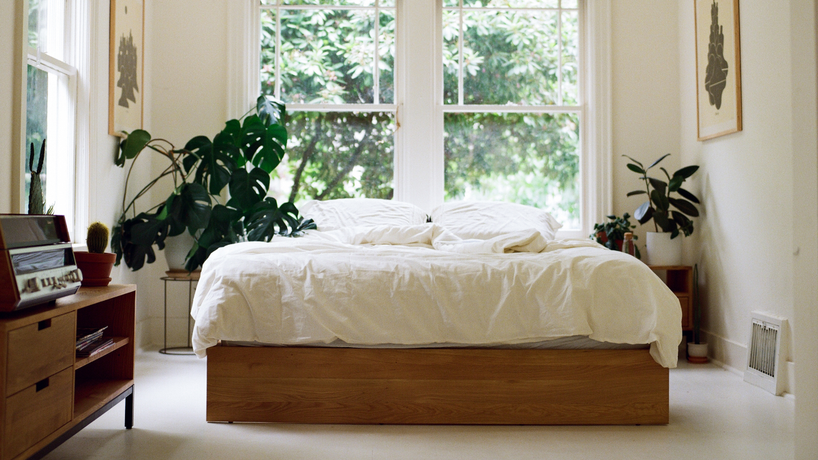 Picture of a room looking at a bed with white bedding on it sitting in front of an open window with trees outside