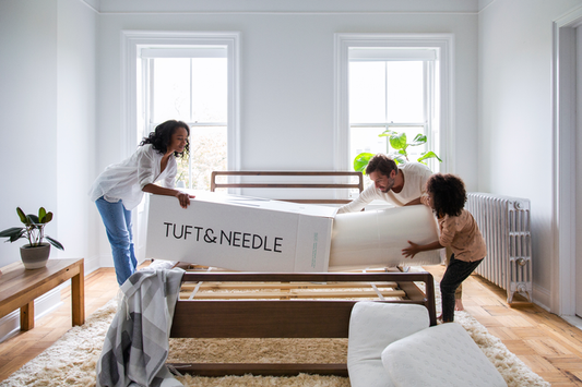 Family of 3 taking their Tuft & Needle Mattress out of the box over their bed frame