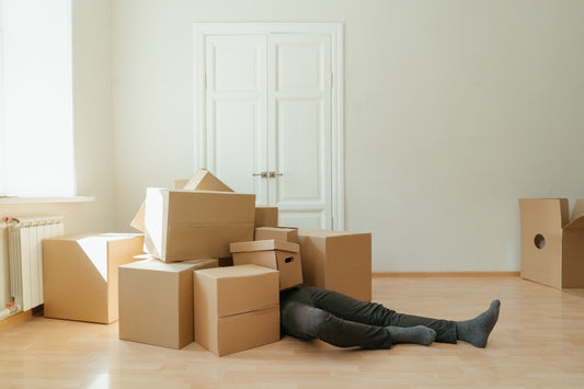 Man laying on the floor under a pile of boxes. All you can see are the stack of boxes and his legs.