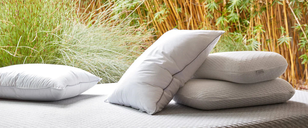 2 white pillows and 2 foam pillows sitting on a white mattress outside with a forest background
