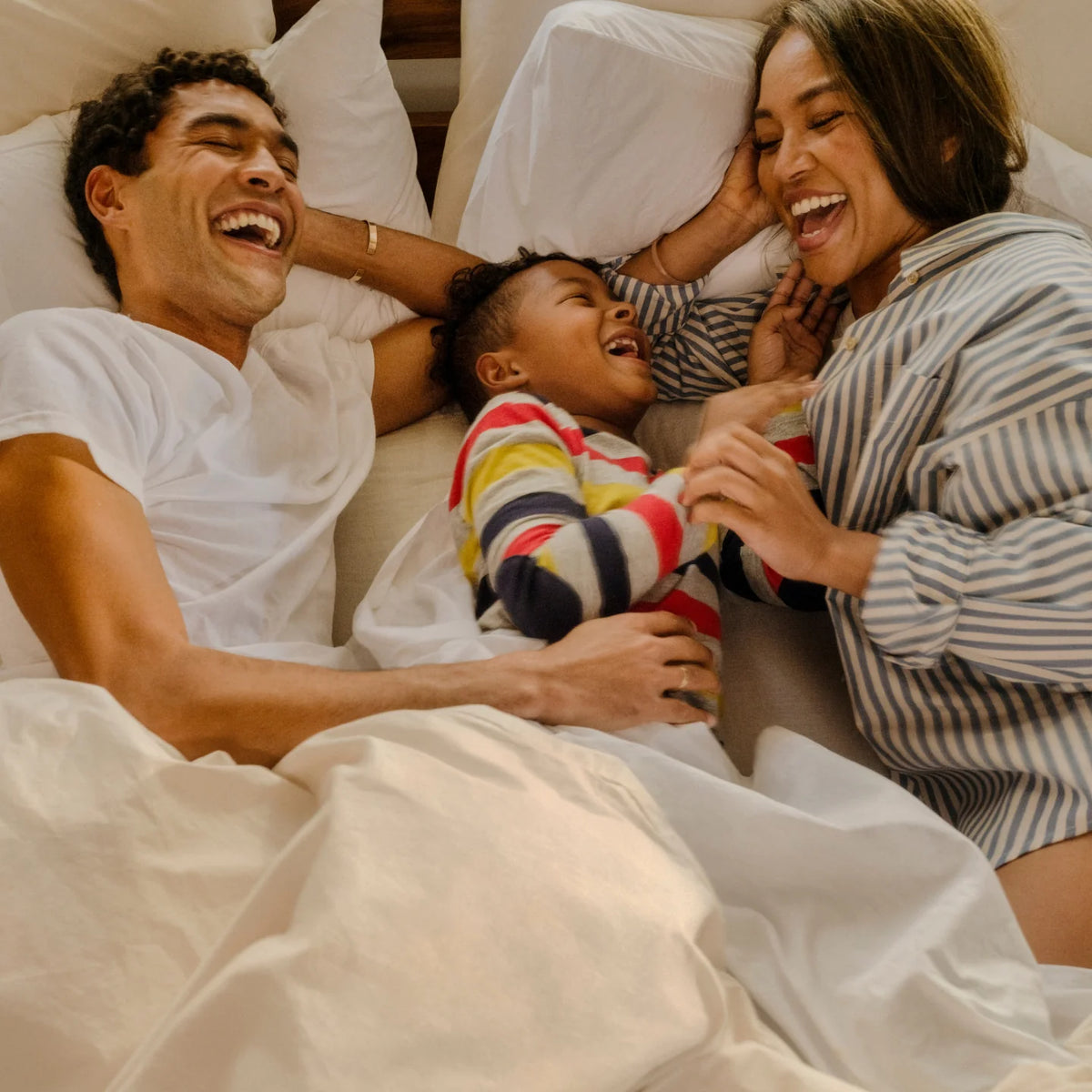 Couple laughs in bed with a small child between them