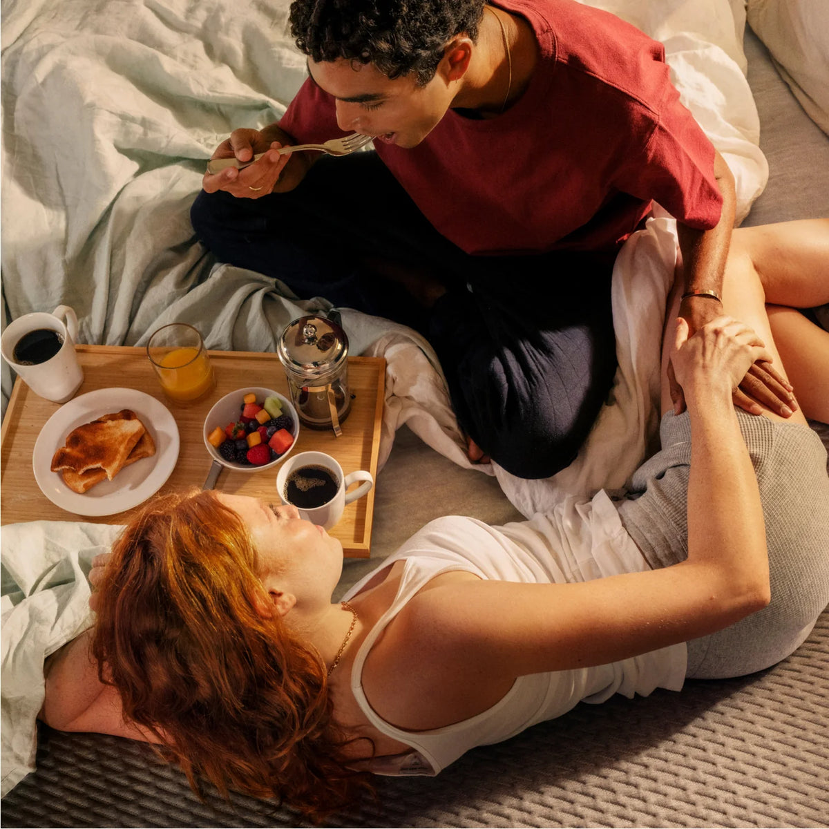Couple lounges in bed while eating breakfast off a tray 