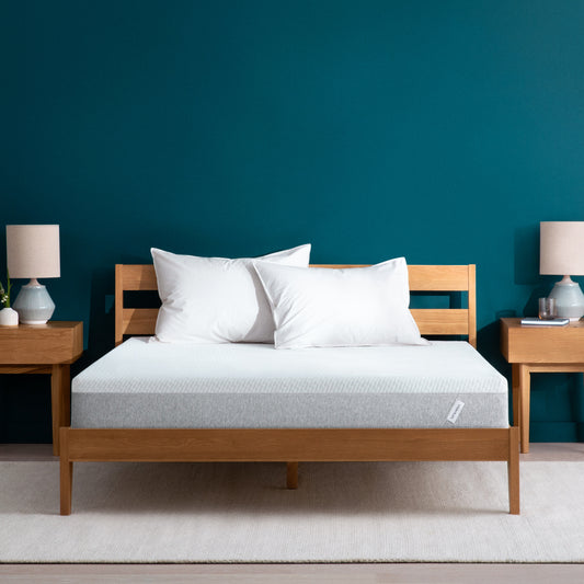 Tuft and Needle Original mattress sitting in a wooden bed frame with two pillows on top of it.