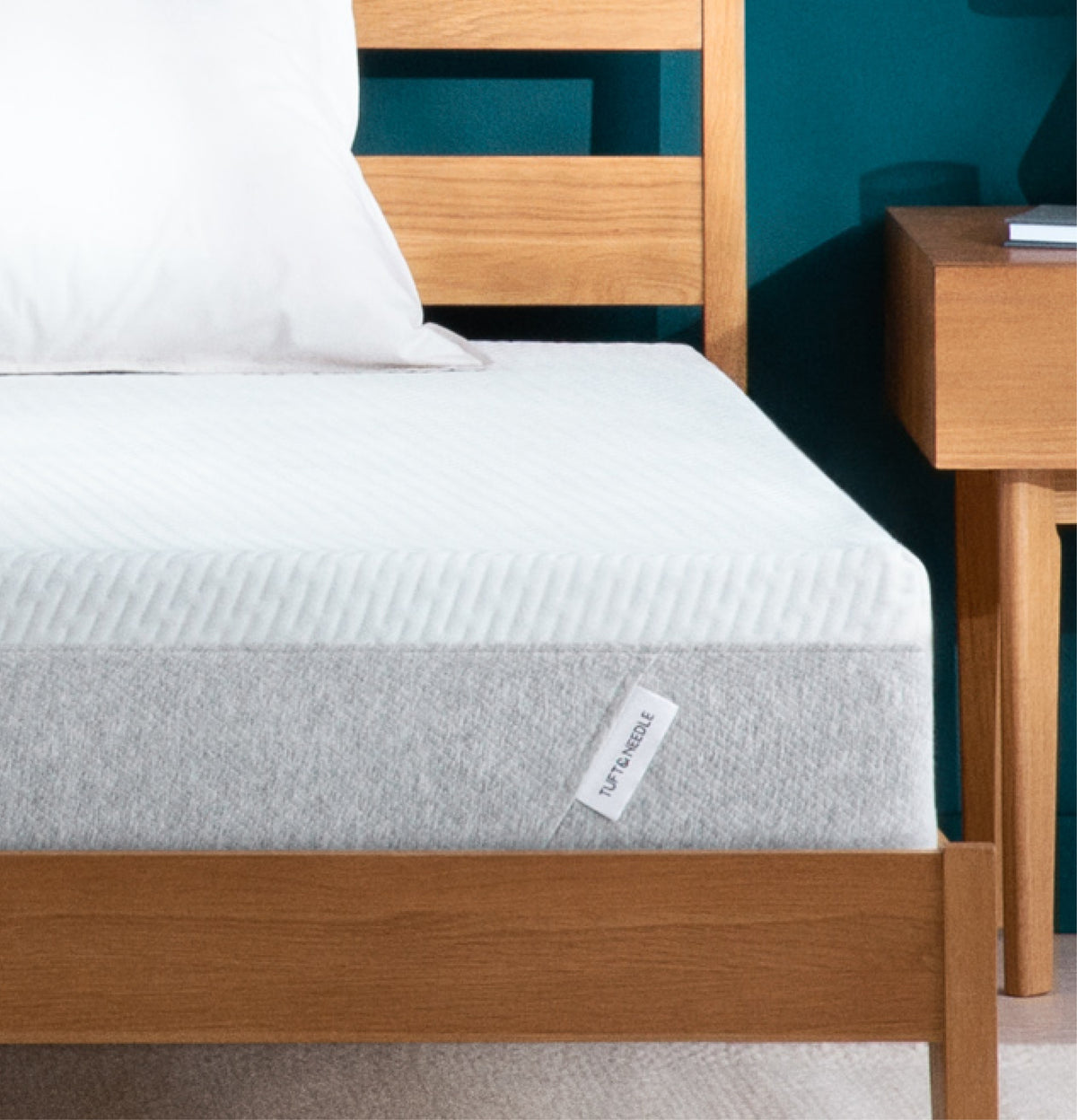 Tuft and Needle Mattress with a visible brand label on a wooden bed frame against a teal wall.