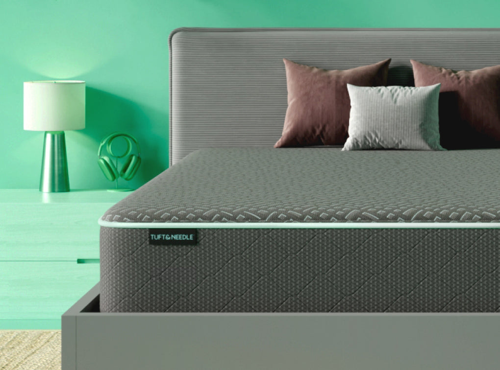 Tuft and Needle Mint mattress II sitting on a white wood bedframe with 3 pillows on top of it.