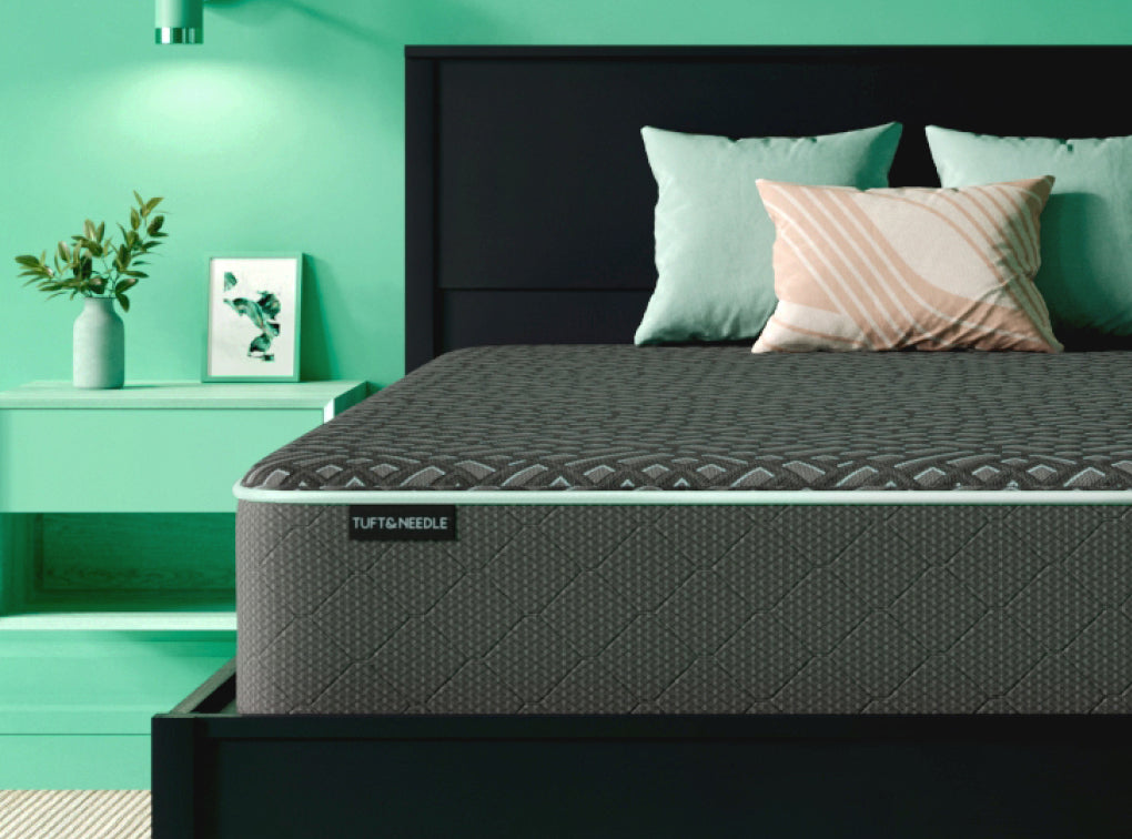 Tuft and Needle Mint Hybrid Luxe mattress sitting on a white wood bedframe with 3 pillows on top of it.