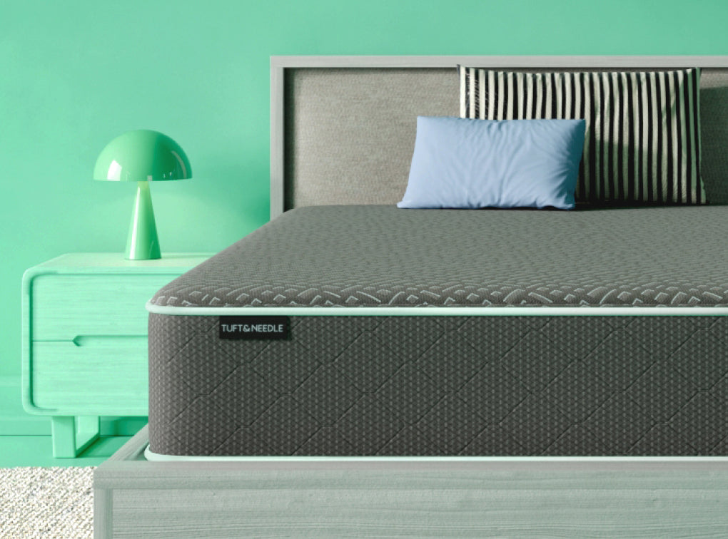 Tuft and Needle Original mattress II sitting on a grey bedframe with 2 pillows on top of it.