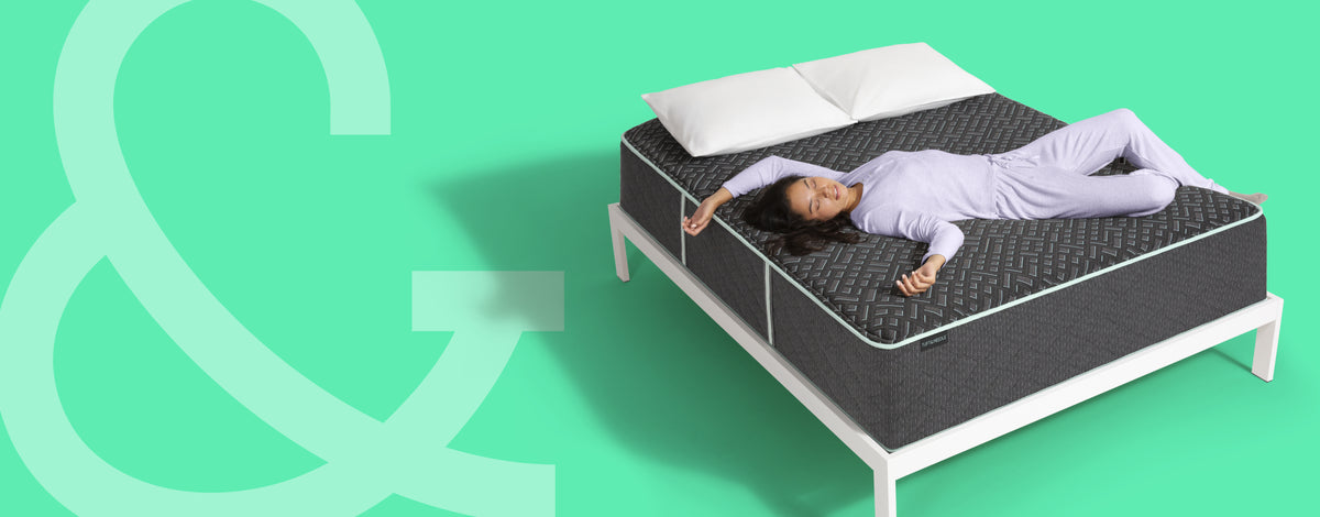 Woman laying on top of a Tuft and Needle Mint Hybrid lux mattress sitting on a white wood bedframe with 2 pillows on top of it.