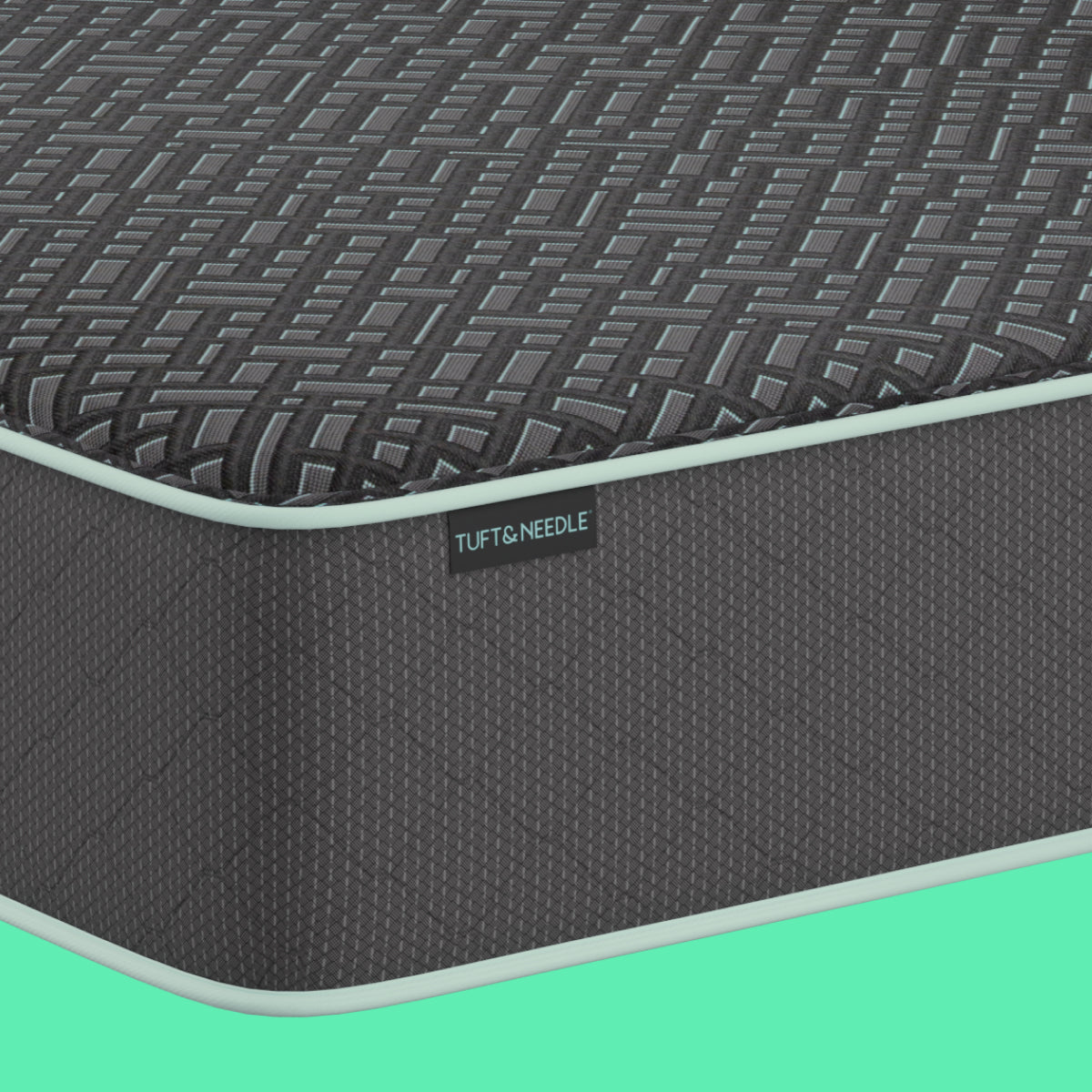 A close-up of a gray Tuft and Needle mattress against a solid mint green background