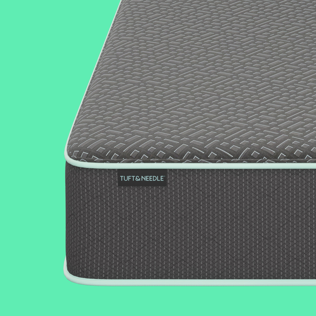 Close-up corner view of a the Tuft and Needle 13.5 inch Mint mattress II showing a dark gray textured top surface and side panel with a visible TUFT & NEEDLE label, set against a solid mint green background.