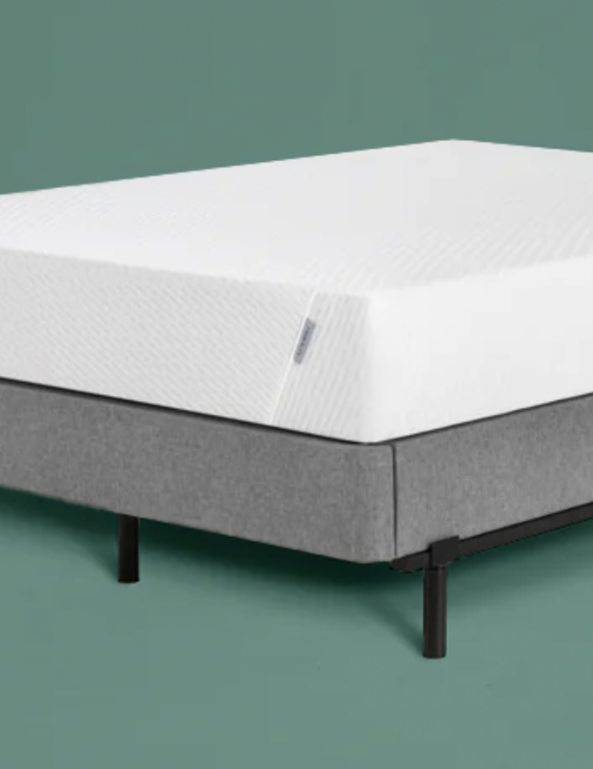 Tuft & Needle mattress on a gray upholstered platform bed frame against a green wall.