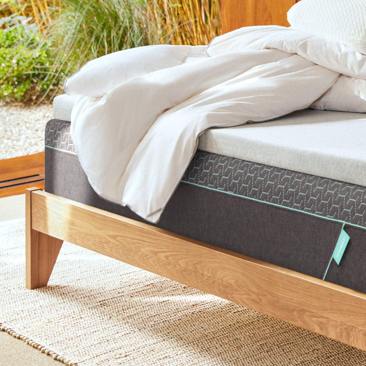 Tuft and Needle Mattress on a wooden bed frame with white down duvet insert on top with an outdoors background