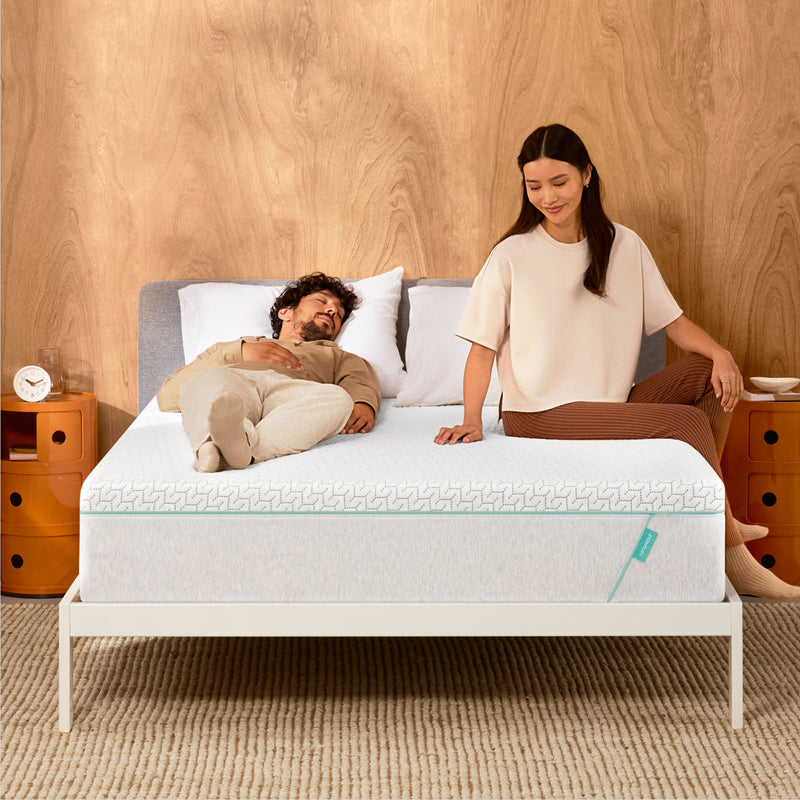 Man and woman laying on a Tuft & Needle Original Hybrid mattress sitting in a white bedframe
