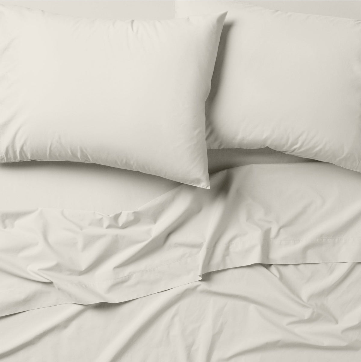 The Tuft and Needle Classic Percale Pillowcase Set, 2 pillows in a pillowcase on top of a spread out sheet || color: Sand

