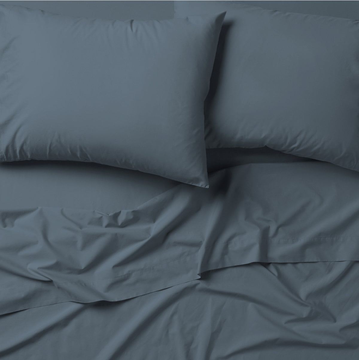 The Tuft and Needle Classic Percale Pillowcase Set, 2 pillows in a pillowcase on top of a spread out sheet || color: Slate
