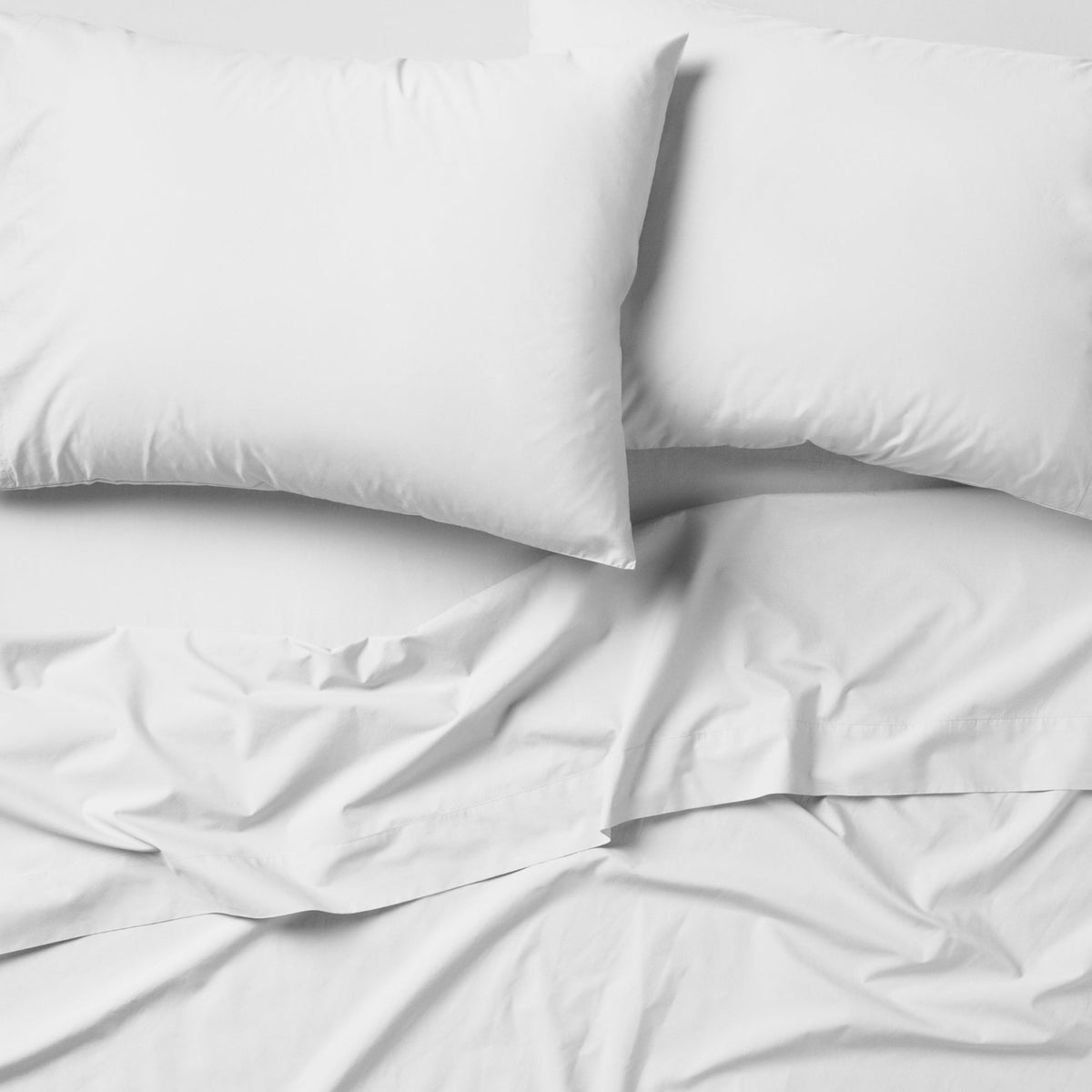 The Tuft and Needle Classic Percale Sheet Set, 2 pillows on top of a sheet on a mattress || color: Cloud
