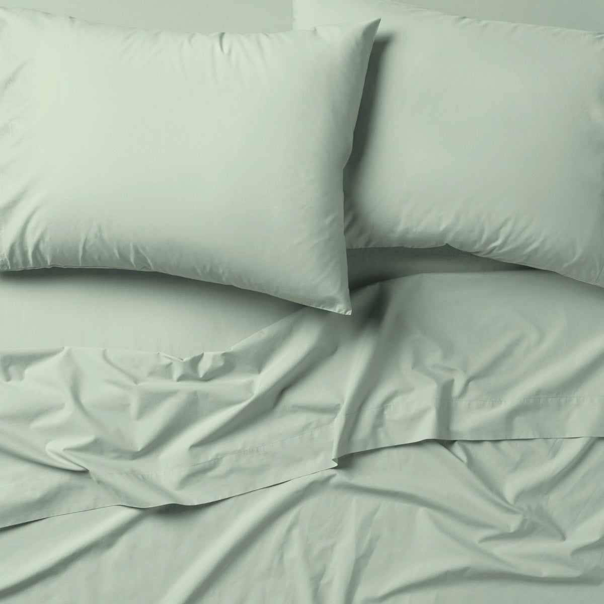 The Tuft and Needle Classic Percale Sheet Set, 2 pillows on top of a sheet on a mattress || color: Sage
