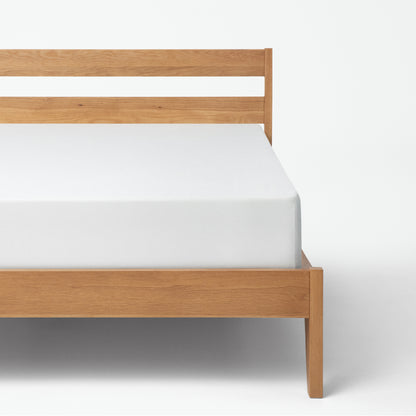 Tuft & Needle Wooden bed frame with white mattress on a white background