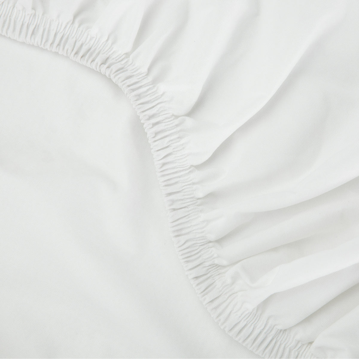  Close-up of a Tuft & Needle white fitted sheet with elastic waistband on a bed.